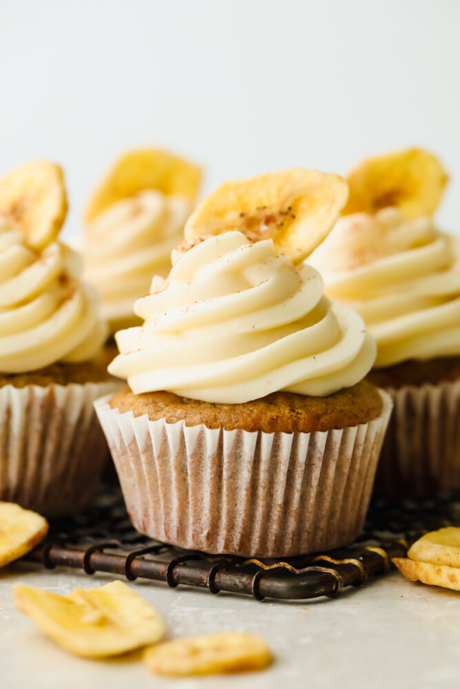 Banana cupcakes with cream cheese frosting topped with a single, dried banana. 