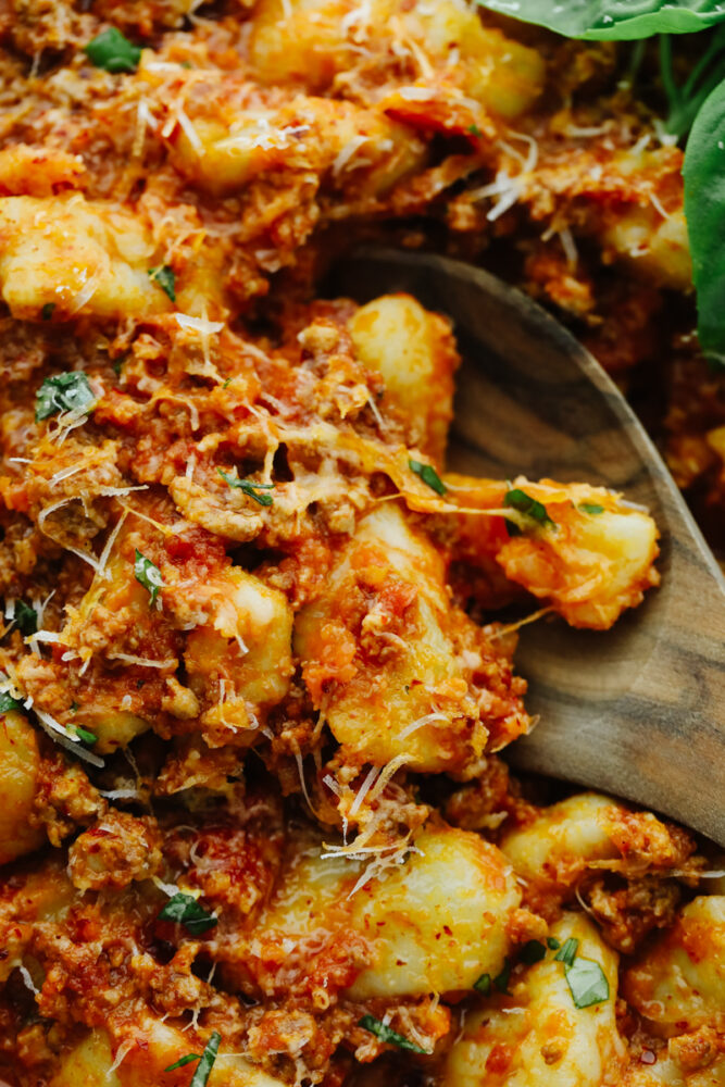 Zoomed in on bolognese gnocchi with a wooden spoon. 