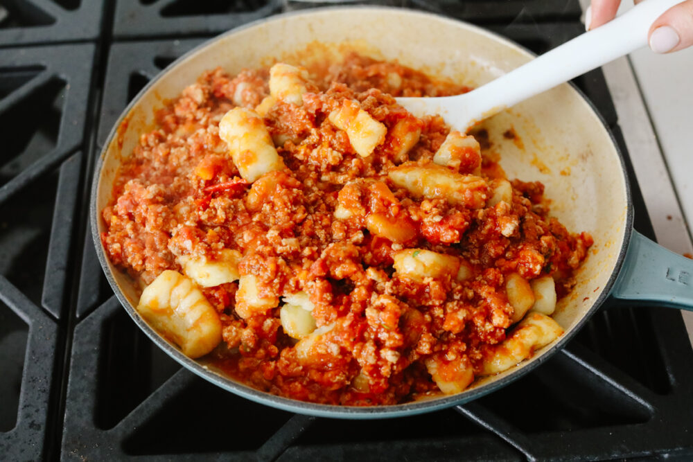 Bolognese Gnocchi is everything that you would hope for in an amazing Italian dish! Flavorful, bold, and full of delightful texture, this tried and true recipe is something that will definitely get you a "WOW!" from your family and friends! Gnocchi and sauce being mixed in a pan.
