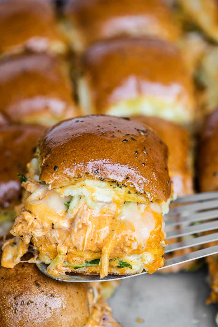 a buffalo chicken slider being lifted out of the pan with a spatula.