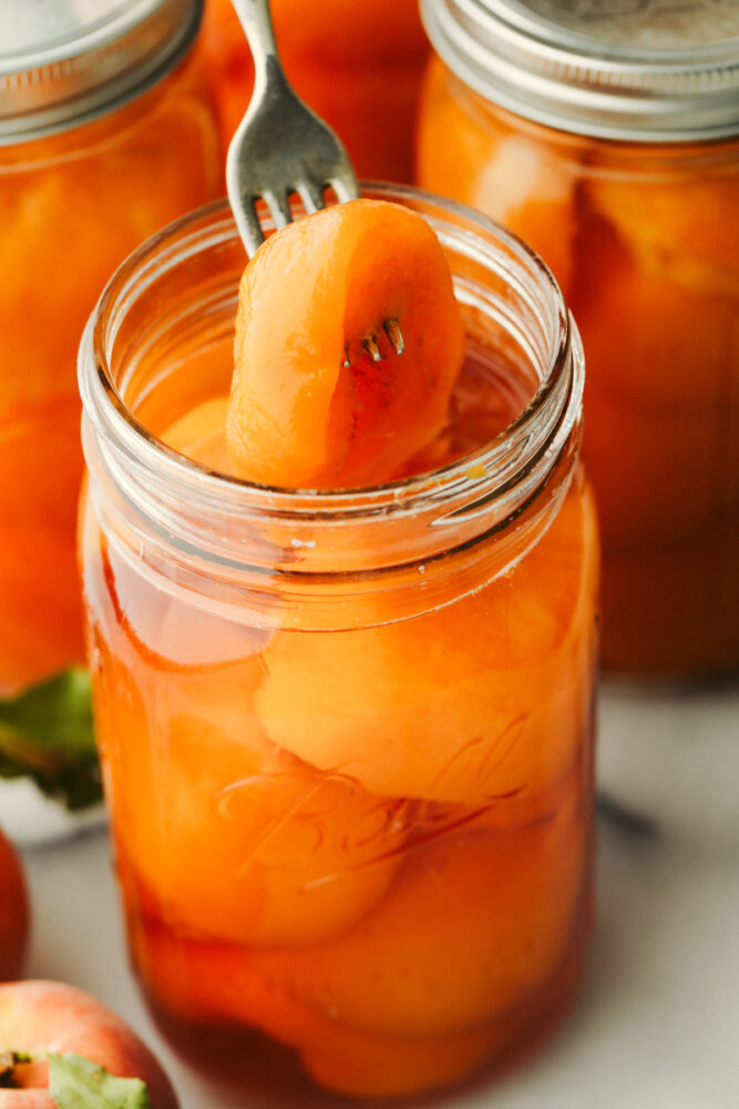 Closeup of canned peaches with a peach skewered on a fork.