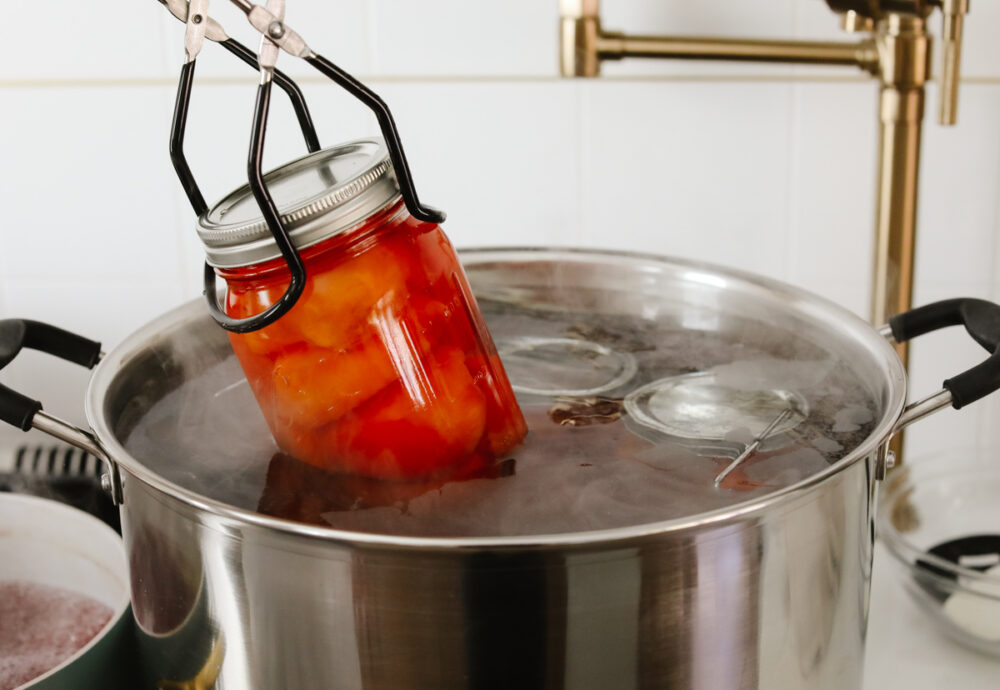 Adding a jar of canned peaches to boiling water for processing.