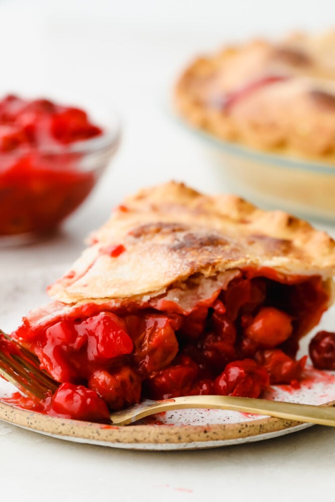 A slice of cherry pie on a plate with a fork. 