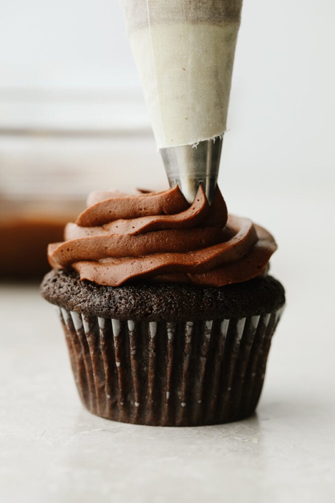 Chocolate buttercream being piped onto a chocolate cupcake.