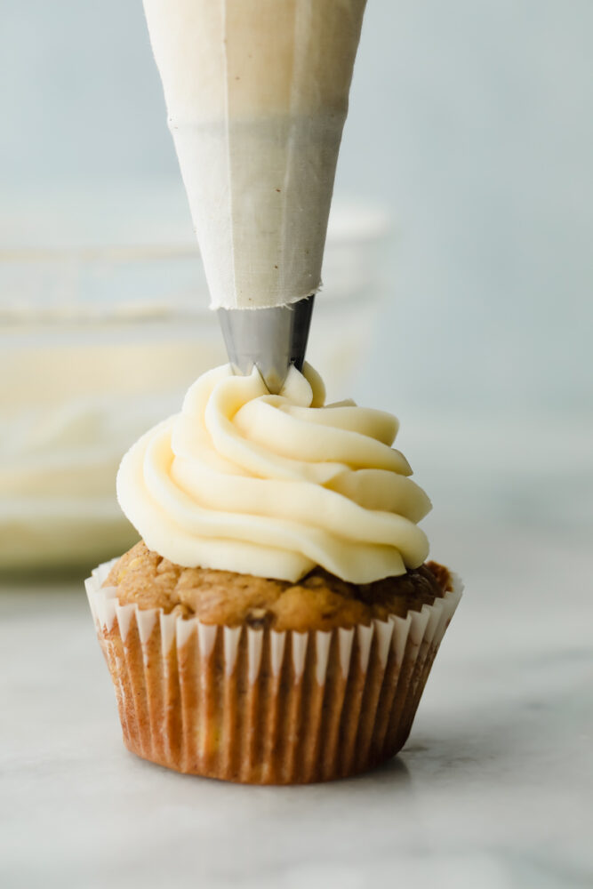 Cream cheese frosting being piped onto a cupcake. 