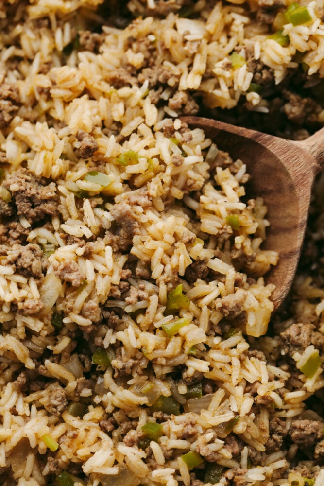 Dirty rice being served with a wooden spoon. 