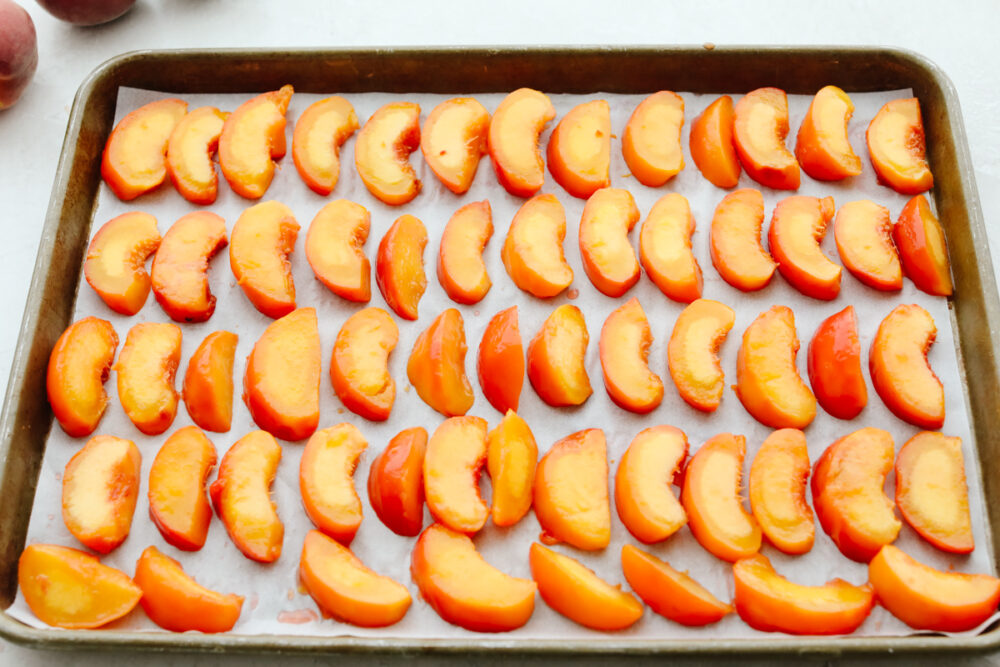 Peaches lined up on parchment paper on a baking sheet. 