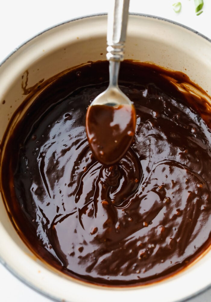Hoisin sauce in a pot, being scooped up with a spoon.