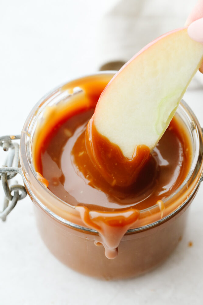 An apple being dipped in caramel sauce. 