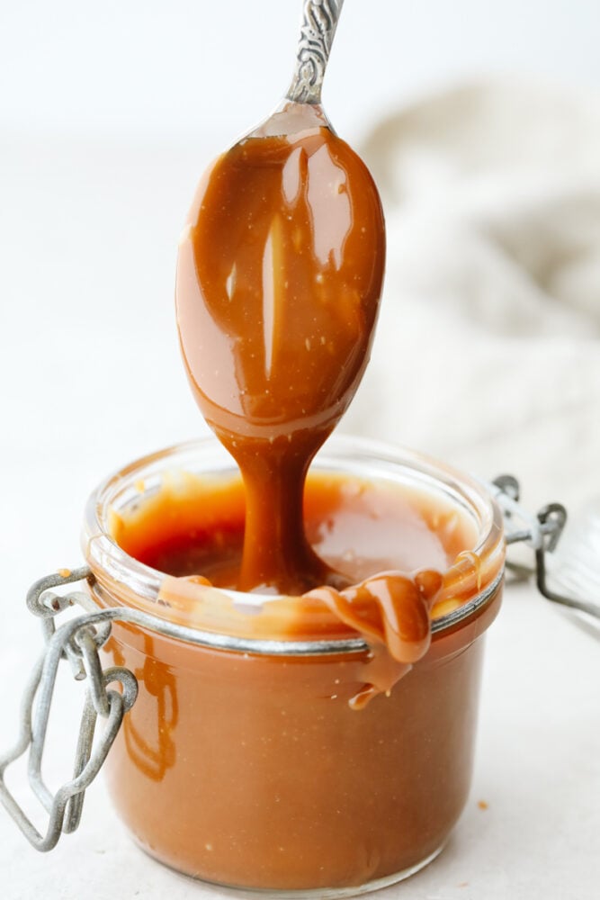 Caramel being dipped into a jar with a spoon. 