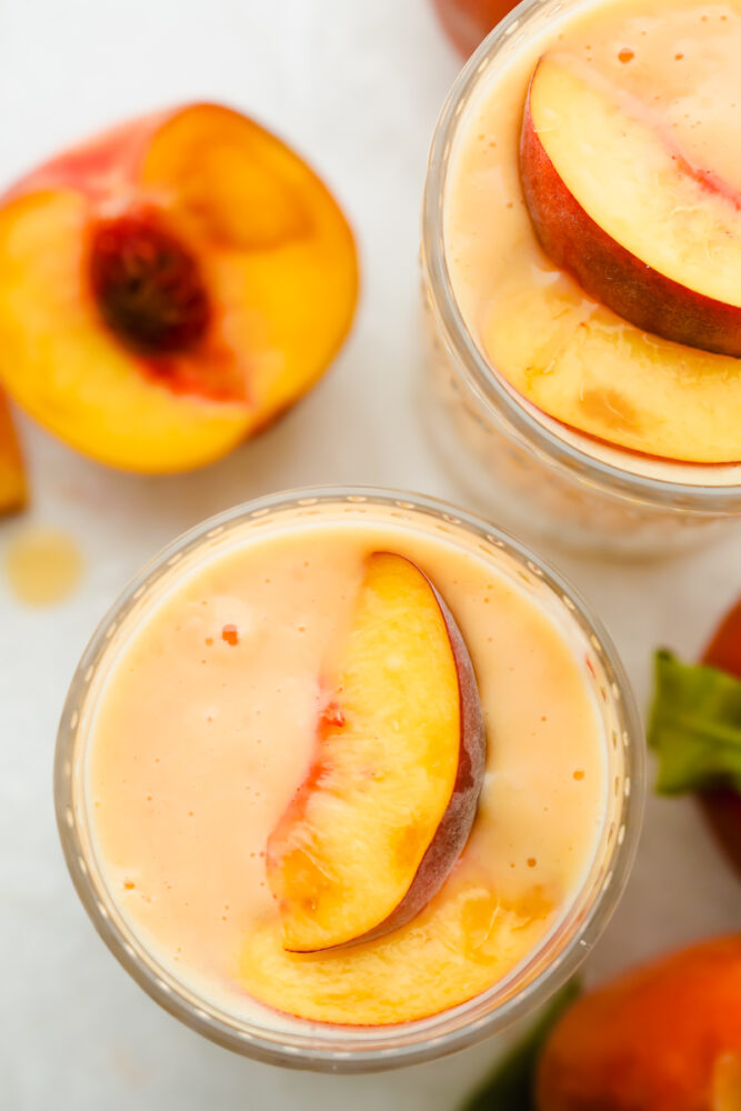 Topview of a peach smoothie with a peach garnishing the top. 