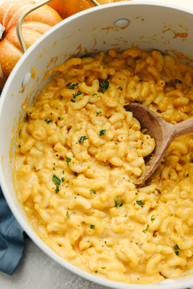 Pumpkin mac and cheese in a large bowl with a wooden serving spoon. 