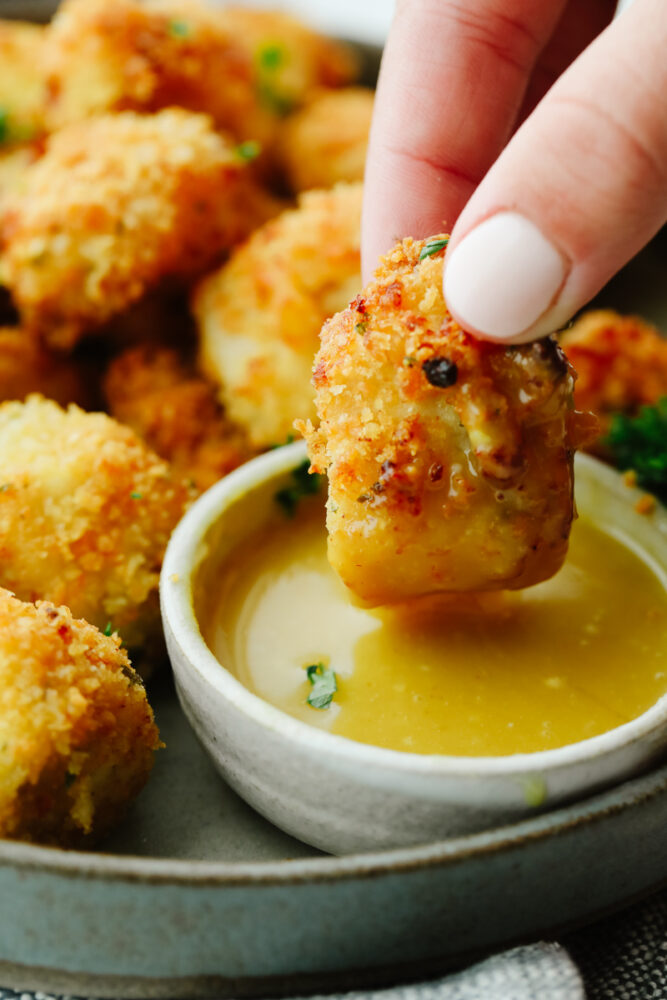 An air fried chicken nugget being dipped into honey mustard sauce.