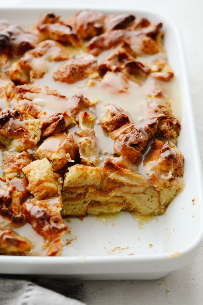 A pan of croissant bread pudding with a piece taken out of the pan. 