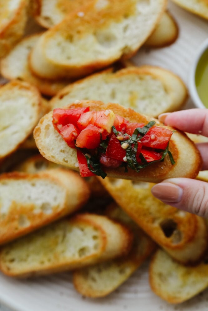 Holding a piece of crostini topped with tomato basil salad.