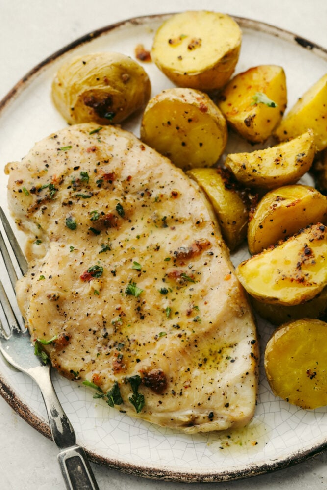 A chicken breast a potatoes on a plate with a fork. 