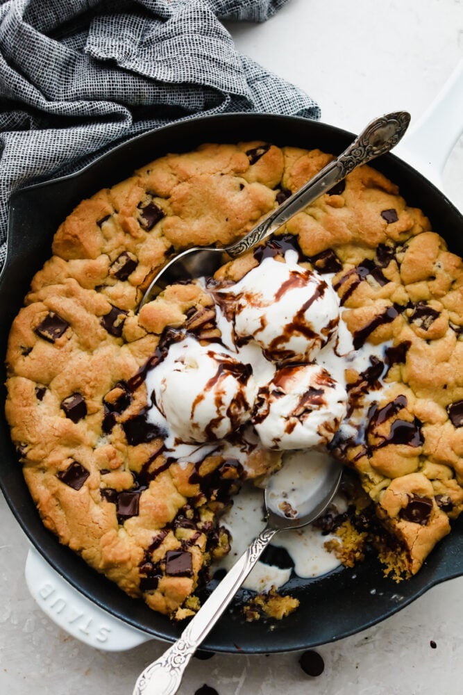 A chololate chip skillet cookie with ice cream on top being eaten with a spoon. 