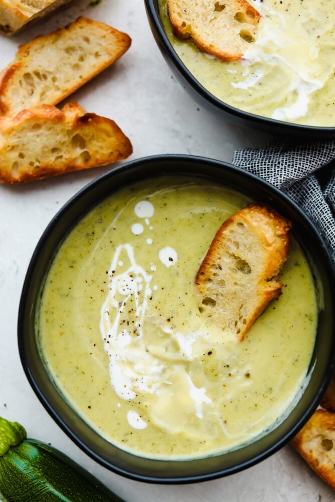2 bowls of zucchini soup drizzled with cream.