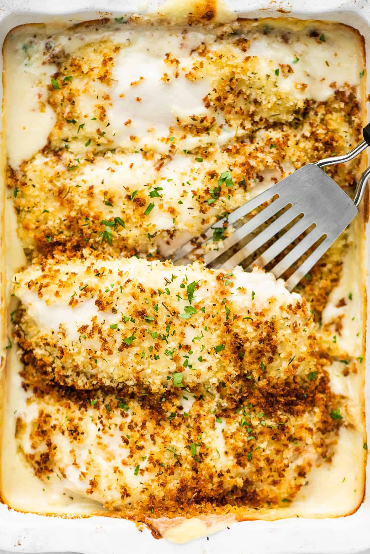 A spatula lifting a piece of creamy Swiss chicken out of a casserole dish.