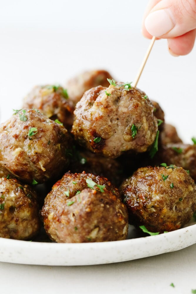 A stack of meatballs with someone putting a toothpick in one of them. 