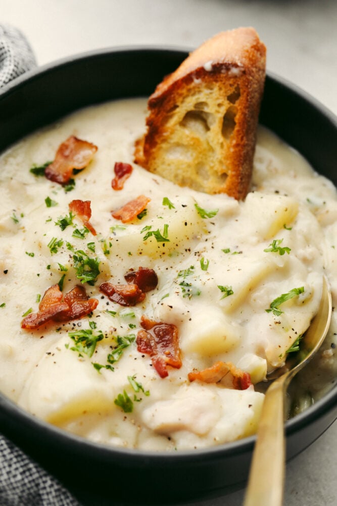 A bowl of clam chowder with a spoon and a crostini. 