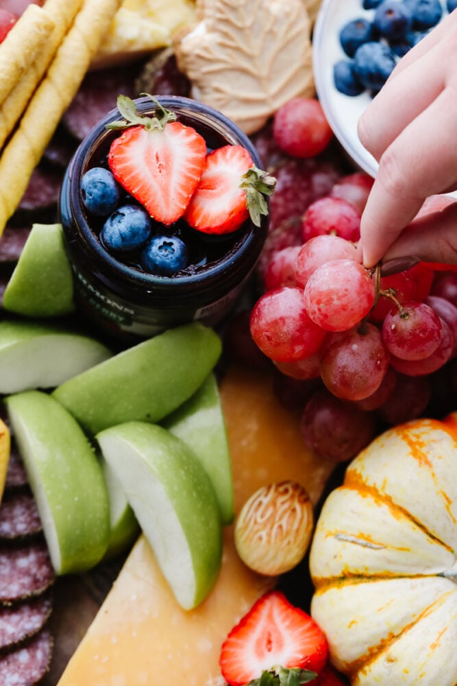 A hand picking up some fruit on a charcuterie board. 