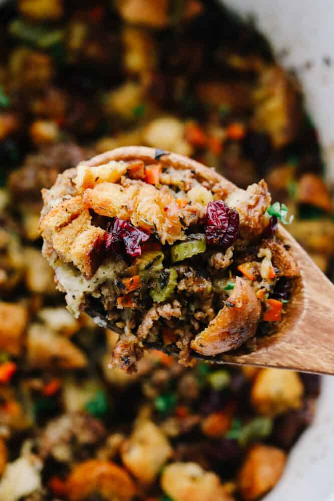 Sausage herb stuffing being served with a wooden spoon. 