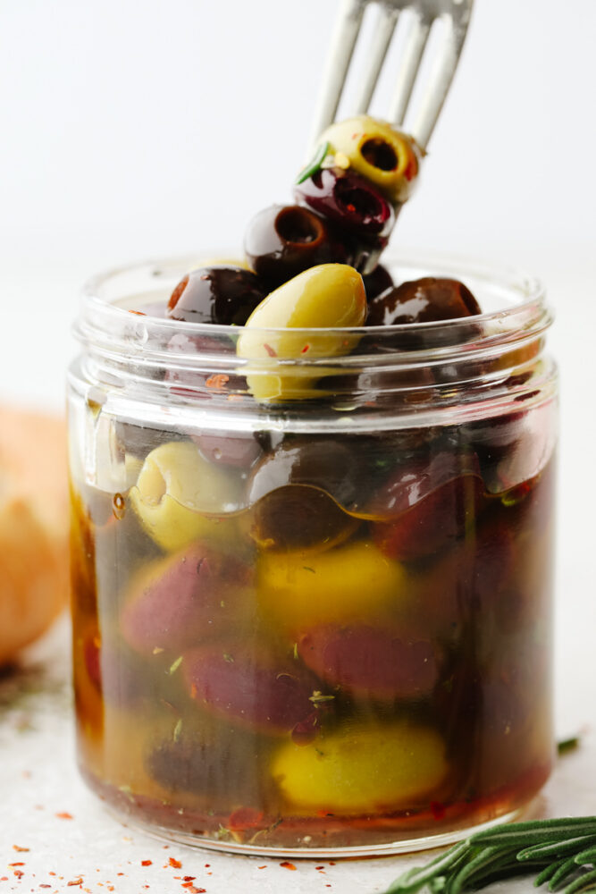A jar of olives in marinade. Skewering 3 on a fork.