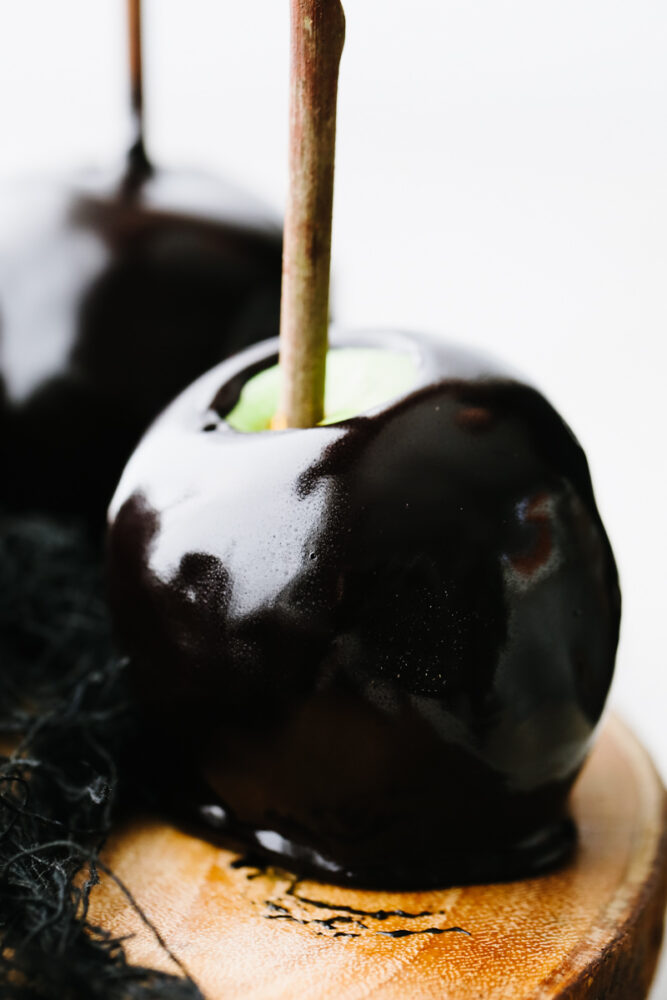 Black caramel apples with a stick on a wooden board. 