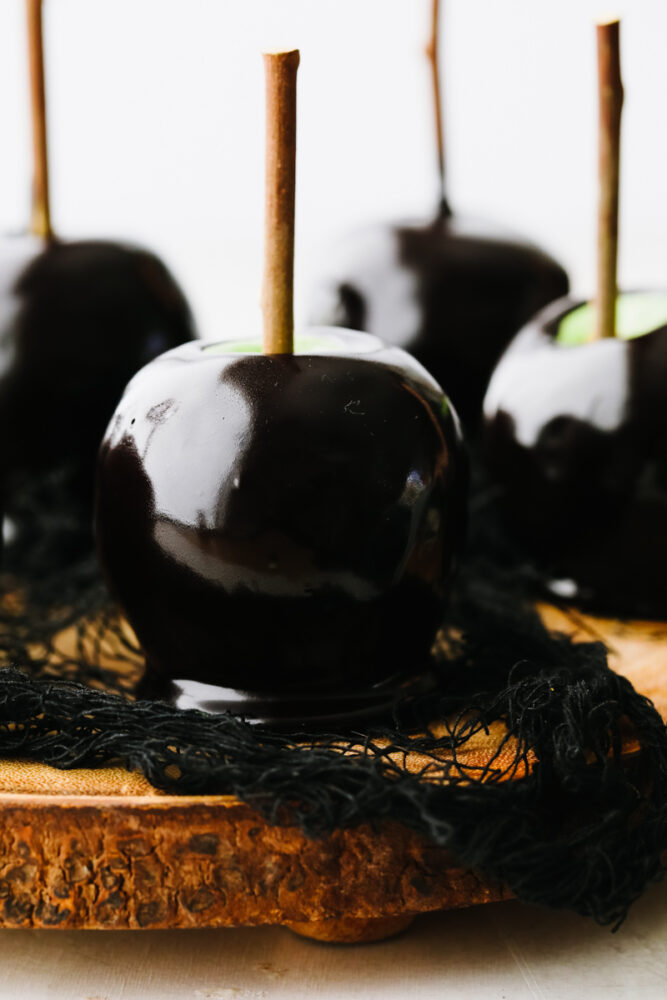 Black caramel apples with sticks gathered together on a wooden board.