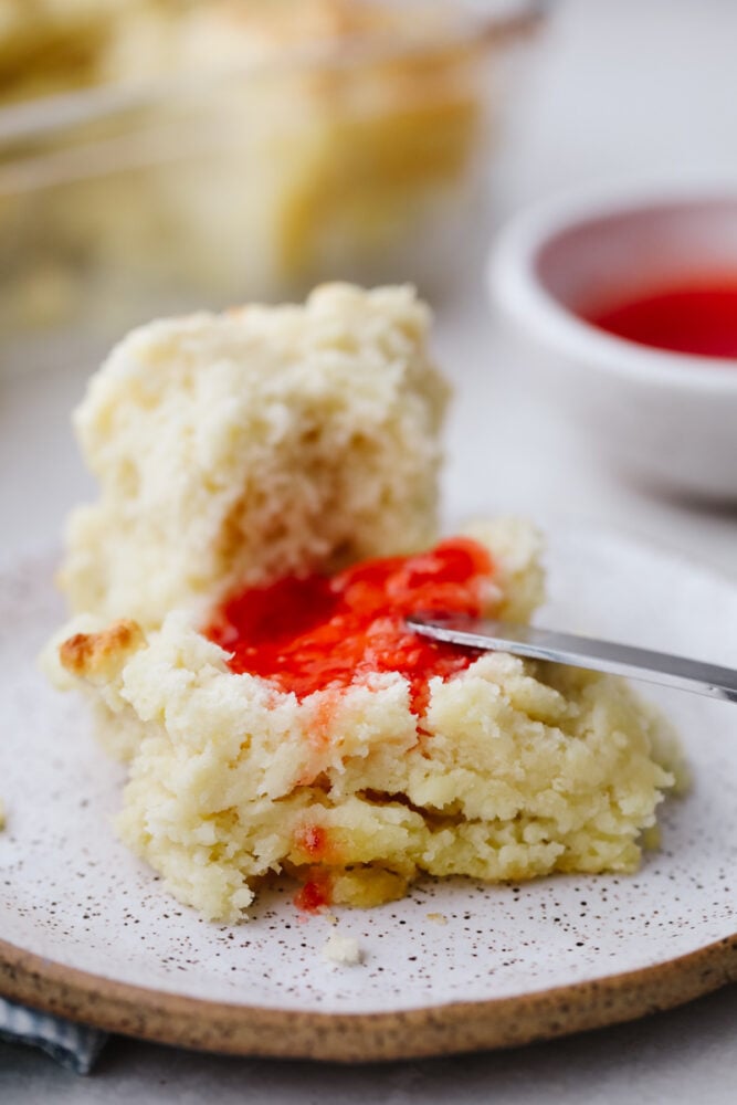 Swim butter biscuit with some strawberry jam being spread on one with a knife. 