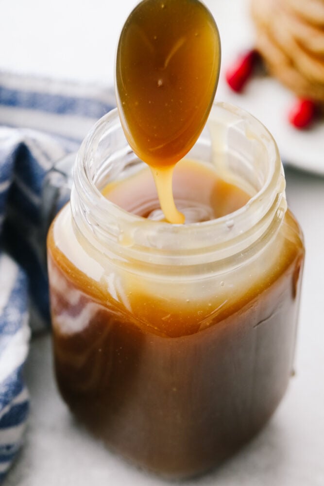 A jar of caramel syrup with a spoon being dipped into it. 