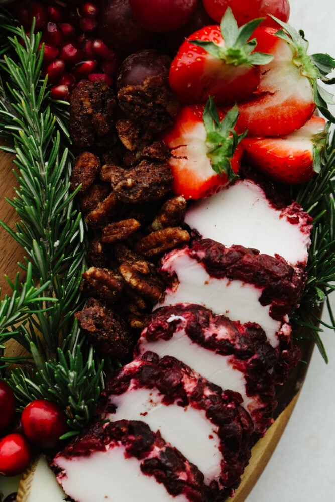 A close up of some cheese, candied pecans, strawberries and a rosemary sprig. 