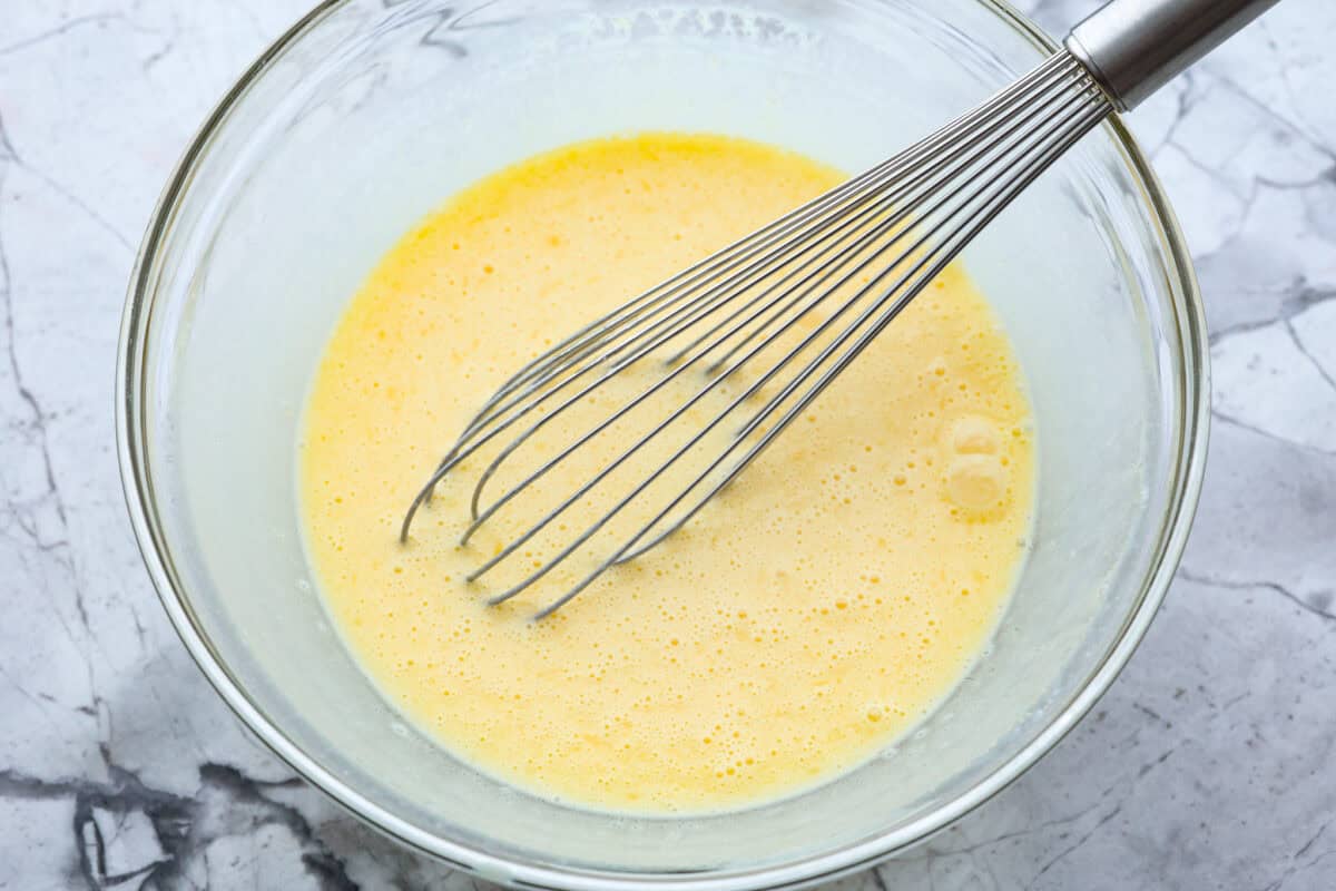 Overhead shot of eggs whisked in a glass bowl. 