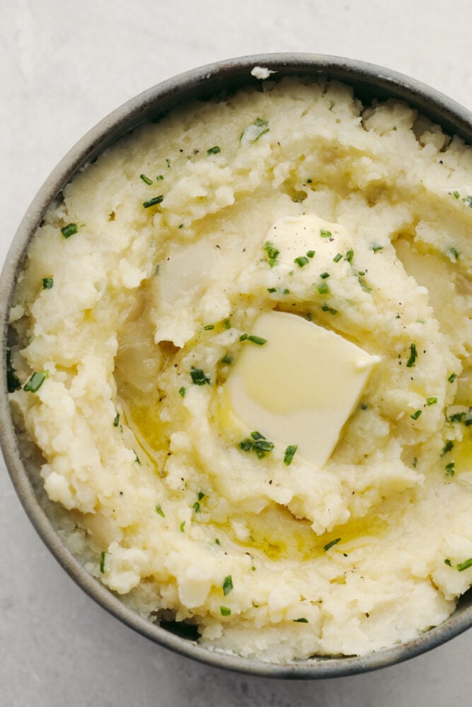 Mashed potatoes in a bowl with some butter and herbs on top. 