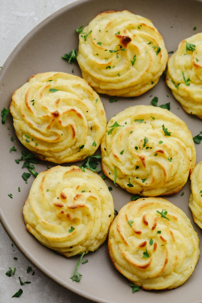 Duchess potatoes garnished with herbs on a gray plate.