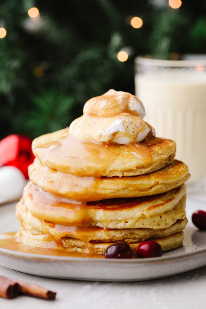 A stack of eggnog pancakes with caramel sauce and whipped cream. 