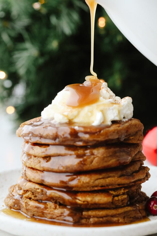 A stack of gingerbread pancakes being drizzled in caramel.