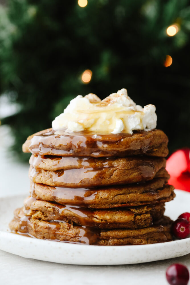A stack of gingerbread pancakes topped with whipped cream and caramel sauce.