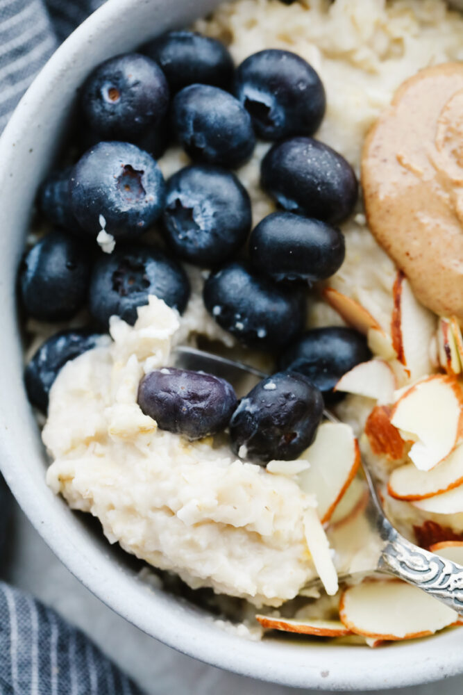 A closeup of oatmeal topped with blueberries, almonds, and nut butter.