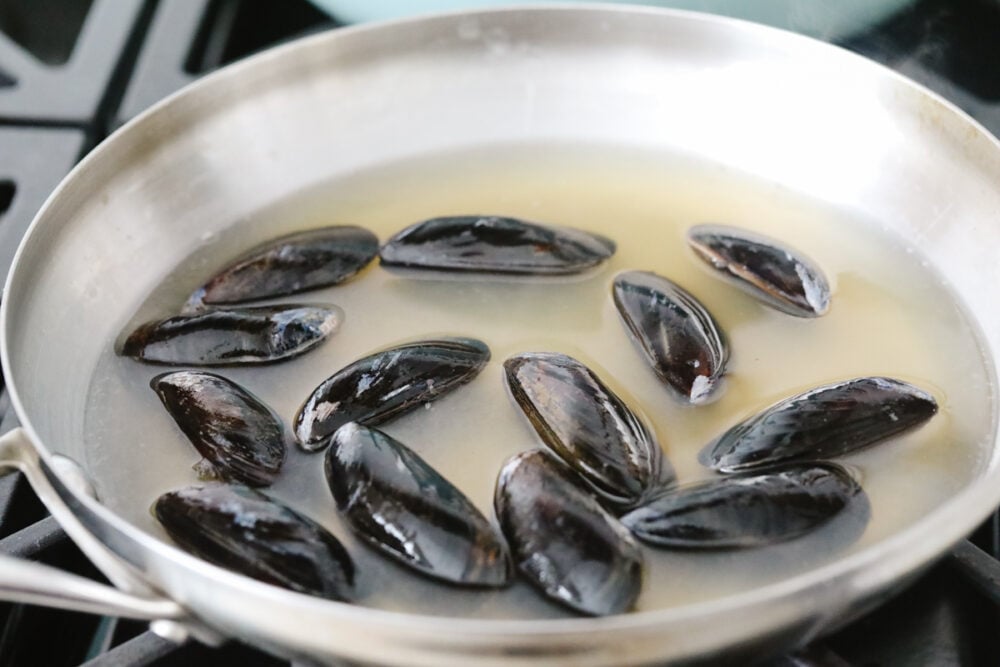 Uncooked mussels in a pan with white wine and chicken broth. 
