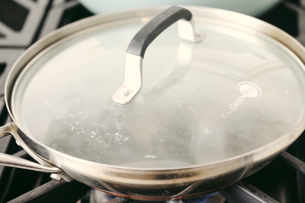 A pan on the stove with a lid that's full of steam. 