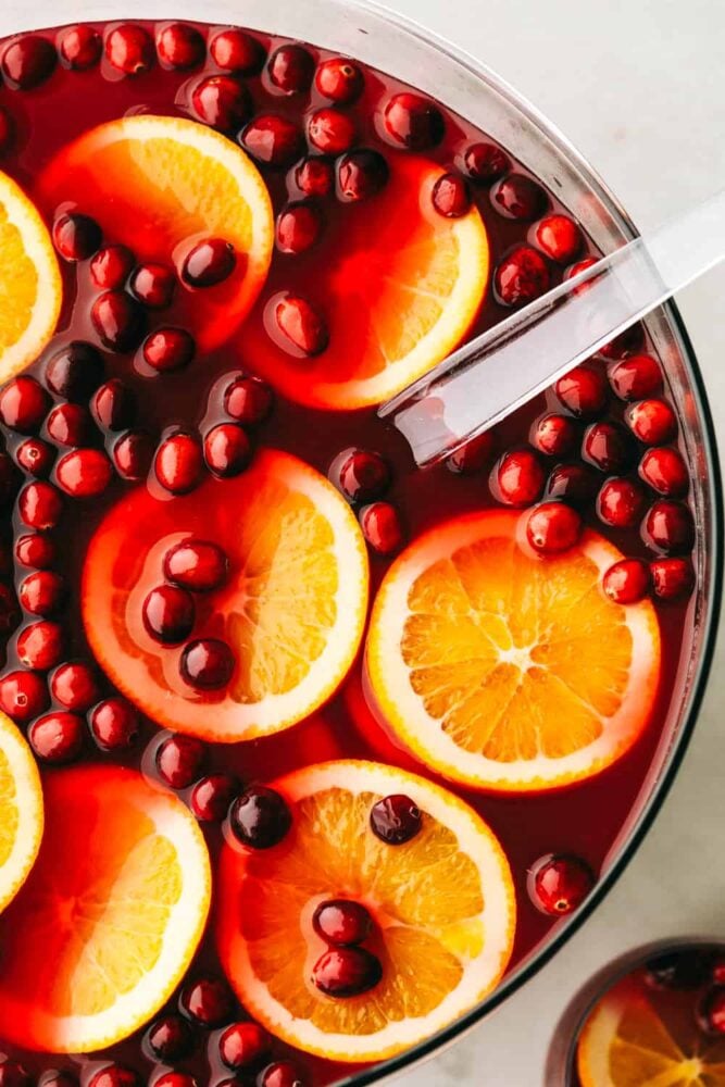 A punch bowl filled with cranberry orange punch that's garnished with orange slices and cranberries. 