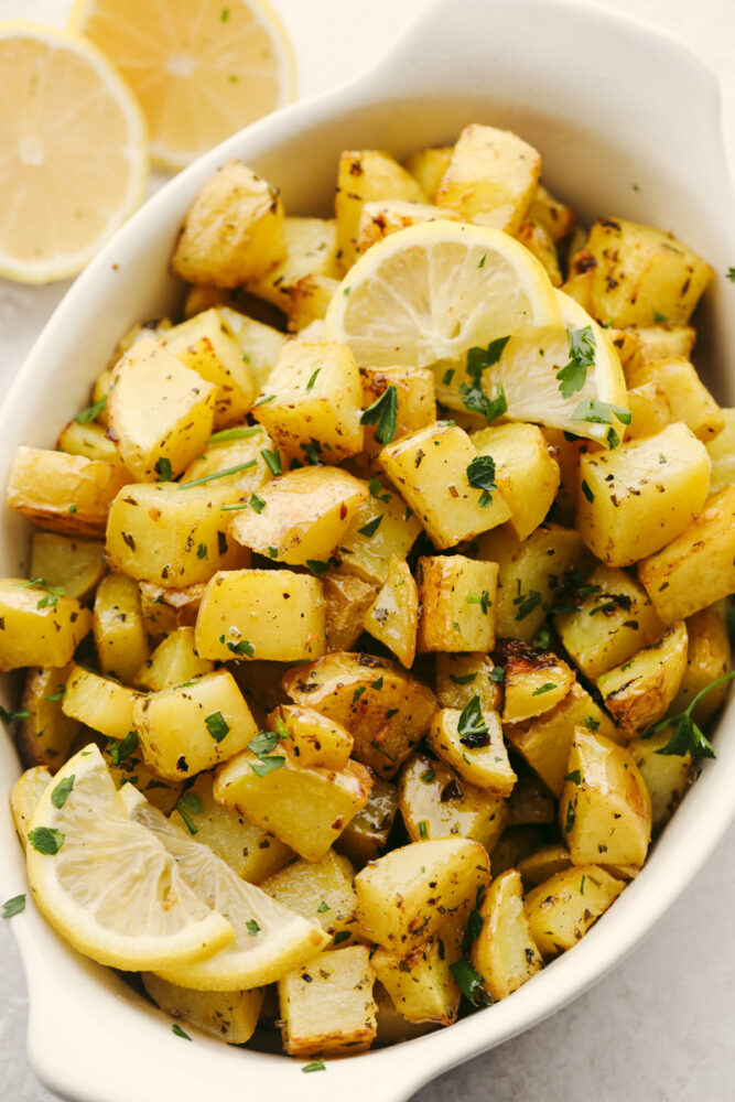 Roasted potatoes in a serving dish garnished with seasonings and lemon slices. 