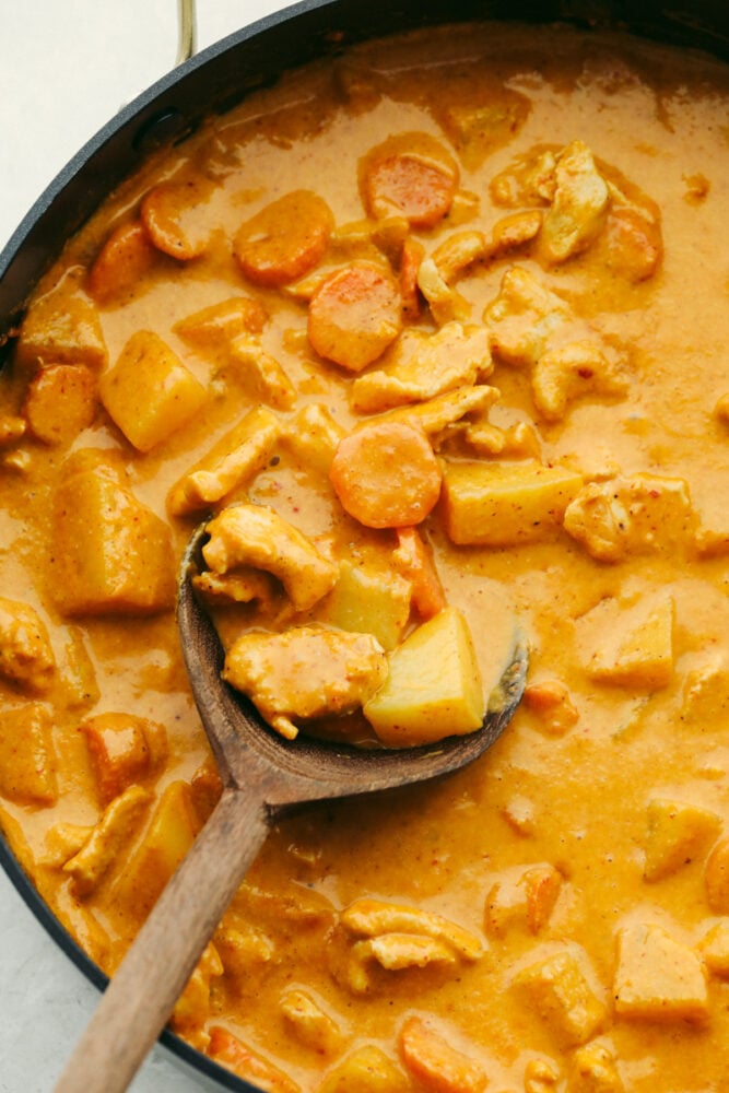 Massaman curry in a pan being scooped with a wooden spoon. 