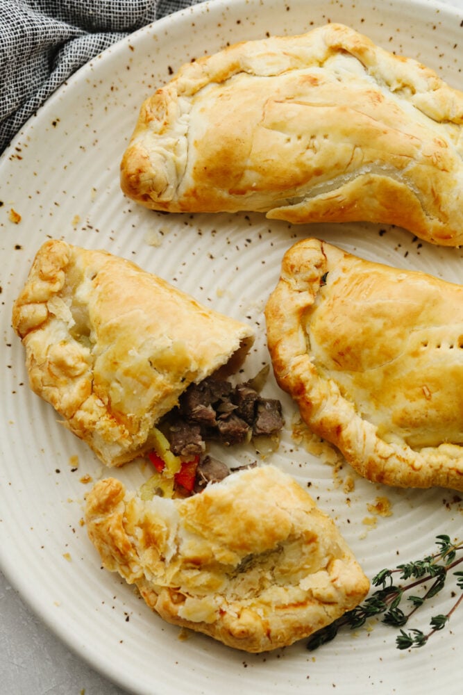 A few cornish pasties on a plate. One has been cut open. 