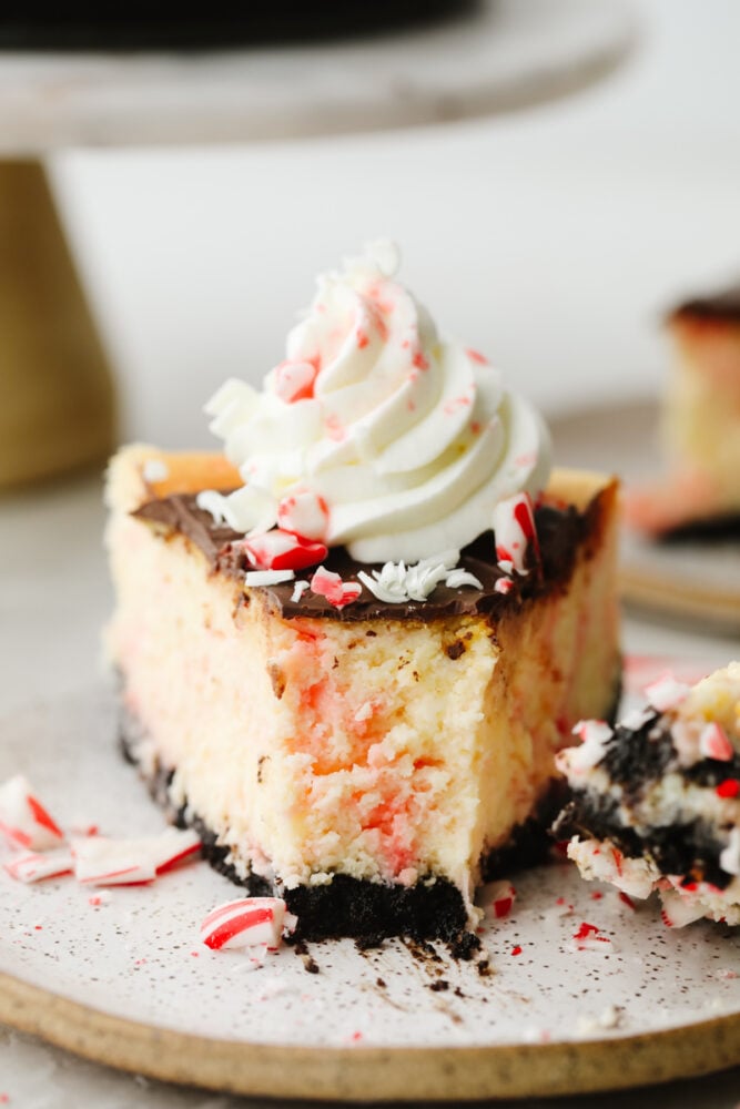 A slice of peppermint cheesecake on a plate with a bite taken out of it. 