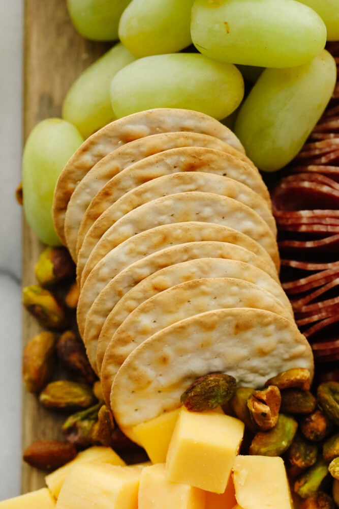 A picture of crackers and pistachios on a charcuterie board. 