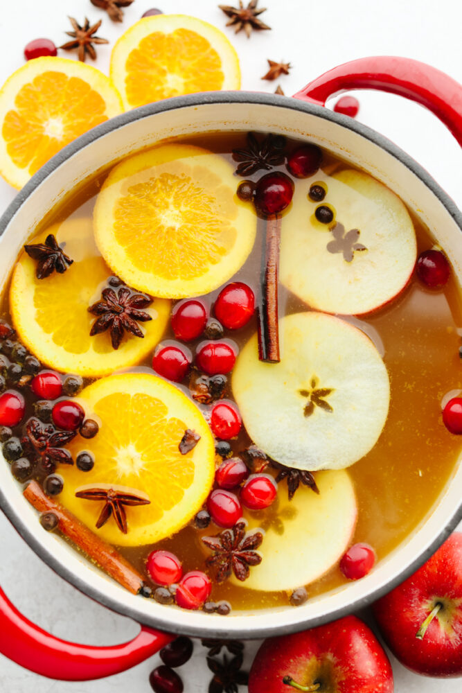 Homemade wassail in a punch bowl garnished with apples, oranges, cranberries, and spice.