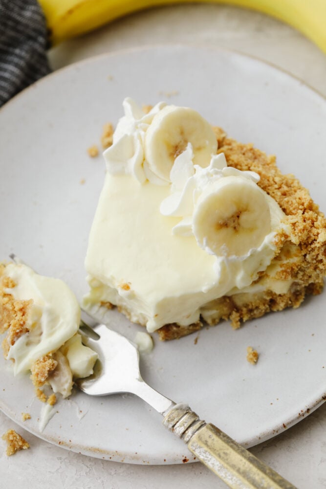 A slice of banana cream cheesecake with a fork cutting a bite. 
